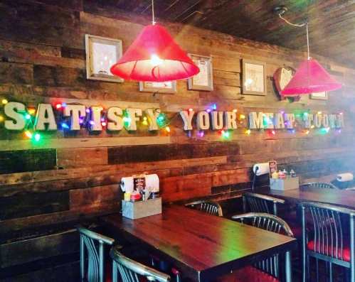 Cozy restaurant interior with wooden walls, colorful lights, and a sign reading "Satisfy Your Meat Tooth."