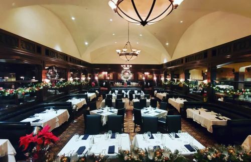 Elegant restaurant interior decorated for the holidays, featuring tables set with white linens and festive greenery.