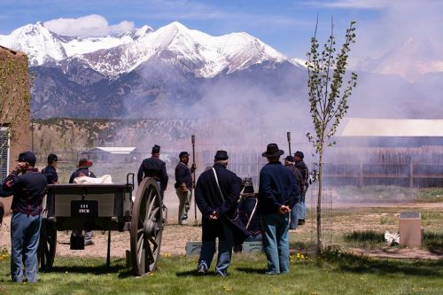 Civil War reenactors firing a cannon with snowy mountains in the background and smoke rising in the air.