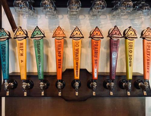 A row of colorful beer taps with unique labels, showcasing various craft beers in a bar setting.