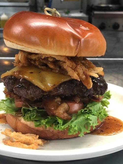 A towering burger with a juicy patty, melted cheese, crispy onions, lettuce, and a glossy bun on a white plate.