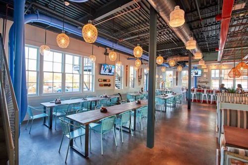 Bright, modern restaurant interior with blue accents, wooden tables, and pendant lights, featuring a spacious dining area.