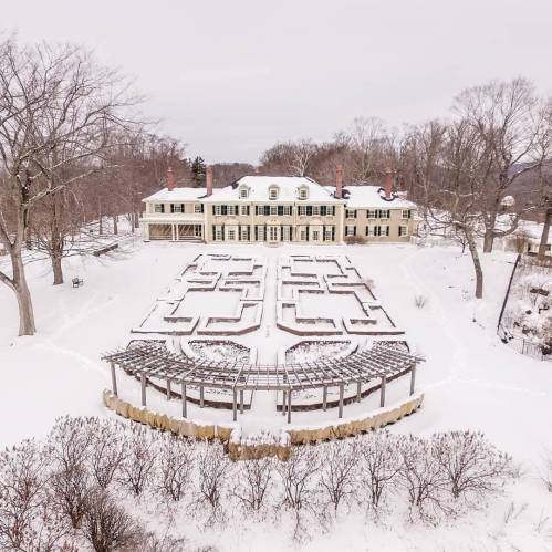 Aerial view of a snow-covered estate with a maze garden in the foreground and a large house in the background.