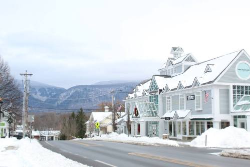 Snow-covered street scene with shops and mountains in the background, creating a serene winter atmosphere.