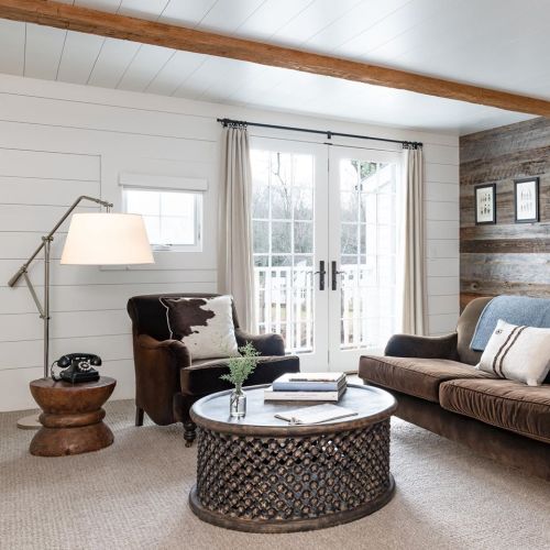 Cozy living room with a brown sofa, armchair, round coffee table, and large windows letting in natural light.