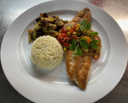 A plate featuring fried fish topped with salsa, served with rice and sautéed Brussels sprouts.