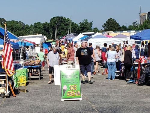 A bustling outdoor market with colorful tents, people browsing, and a sign advertising ice cream.
