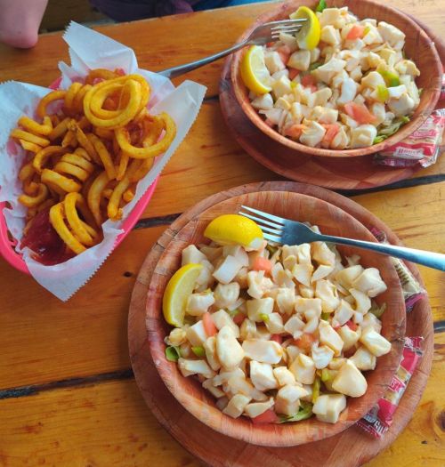 Two wooden bowls of seafood salad with lemon wedges, alongside a serving of curly fries with ketchup.