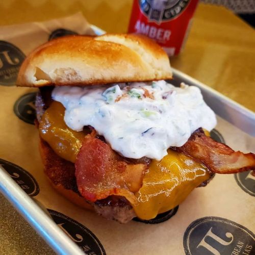 A close-up of a burger with bacon, melted cheese, and creamy sauce on a toasted bun, served on parchment paper.