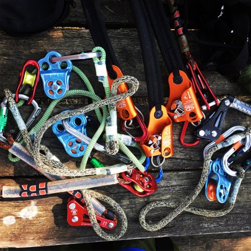 A collection of climbing gear, including carabiners, pulleys, and ropes, arranged on a wooden surface.
