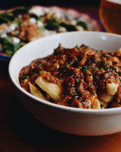 A bowl of hearty dish with chopped potatoes topped with a savory meat sauce and garnished with green herbs.