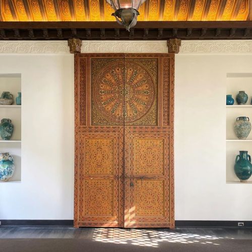 Intricately carved wooden double doors with a circular design, flanked by shelves of decorative blue vases.