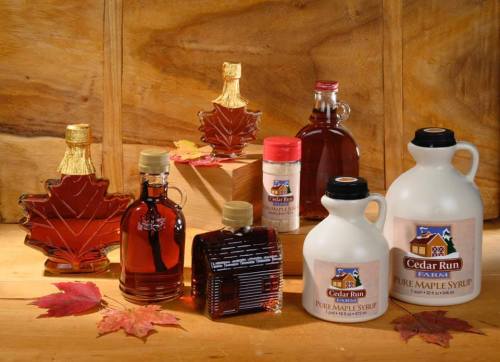 A variety of maple syrup bottles and jars displayed on a wooden surface with autumn leaves.