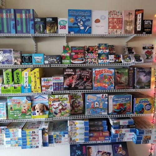 A colorful display of various board games and puzzles on shelves, showcasing a variety of themes and styles.