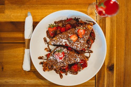 A plate of chocolate-covered croissants topped with strawberries and powdered sugar, served with a drink.