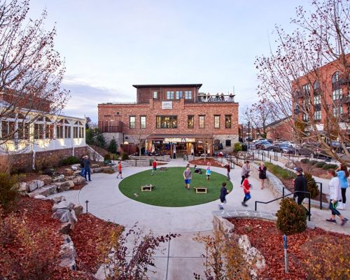 A lively outdoor space with children playing on a green lawn, surrounded by trees and a brick building in the background.
