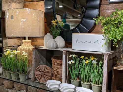 A cozy display featuring a lamp, decorative vases, faux flowers, woven baskets, and a sign that says "bread."