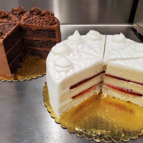 Two cakes on a silver surface: one chocolate layer cake and one white cake with strawberry filling, both decorated with frosting.