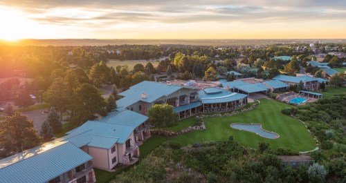 Aerial view of a resort with green lawns, pools, and trees at sunset, showcasing a serene landscape.