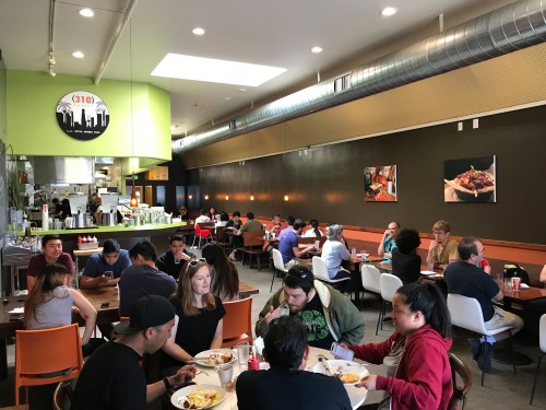 A bustling restaurant interior with diners at tables, enjoying meals in a modern, casual setting.