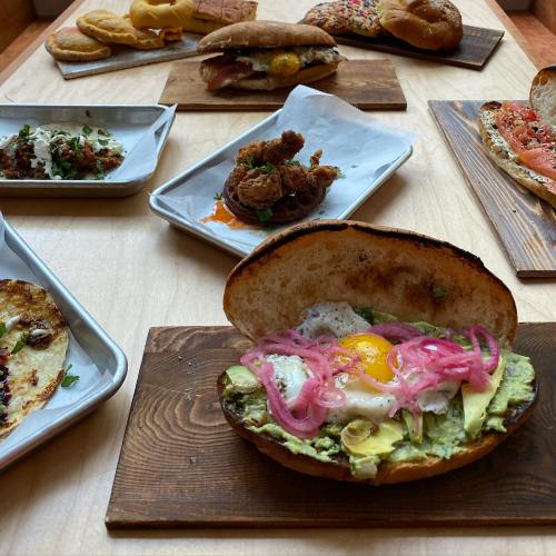 A variety of delicious dishes on wooden boards, featuring sandwiches, tacos, and fried chicken with vibrant toppings.
