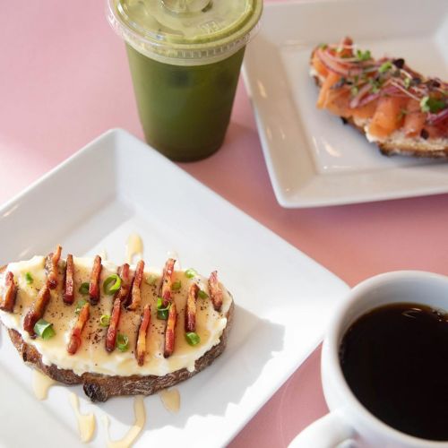 A plate with toast topped with bacon and green onions, a salmon dish, a cup of coffee, and a green drink.