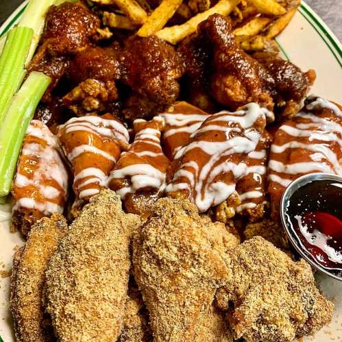 A plate of assorted chicken wings with fries, celery, and dipping sauce, featuring different sauces and coatings.