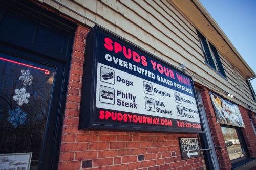 Sign for "Spuds Your Way" featuring menu items: overstuffed baked potatoes, dogs, burgers, Philly steak, milkshakes.