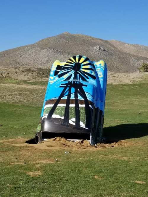 A colorful mural of a windmill on a large, tilted structure in a grassy area with hills in the background.