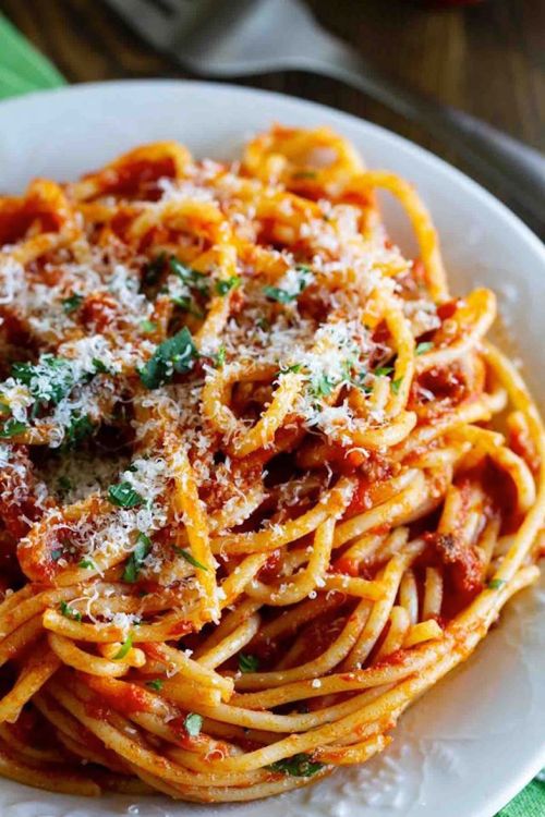A plate of spaghetti topped with marinara sauce, grated cheese, and fresh herbs.