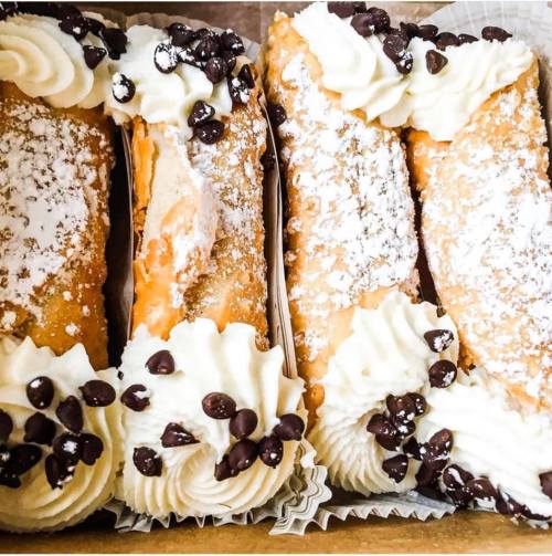 Three delicious cannoli filled with cream, topped with whipped cream and chocolate chips, in a decorative box.
