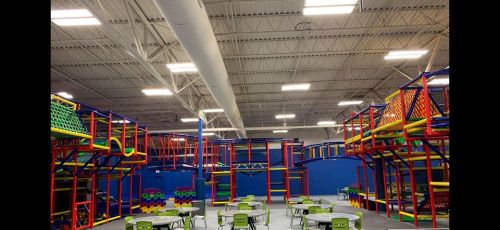 Indoor play area with colorful climbing structures and tables for seating. Brightly lit and spacious environment.