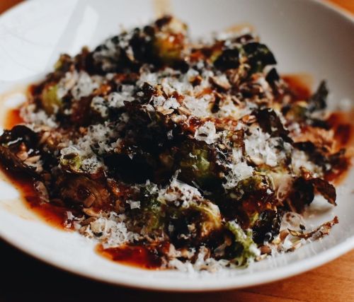 A plate of roasted Brussels sprouts topped with grated cheese and a drizzle of sauce.