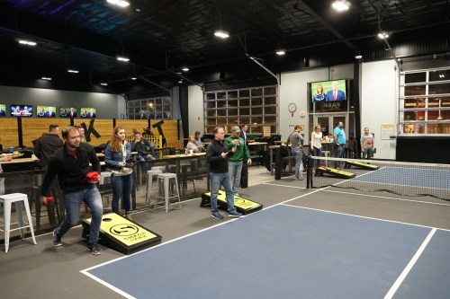 A lively indoor sports venue with people playing games, socializing, and watching TV on large screens.