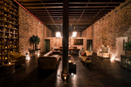 Cozy interior with brick walls, wooden beams, and warm lighting, featuring a leather sofa and elegant decor.