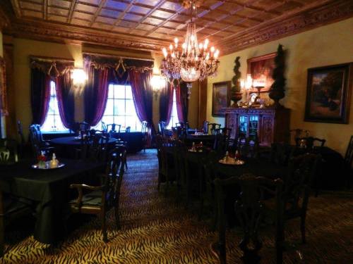 Elegant dining room with dark tables, ornate chandelier, and rich decor, featuring a tiger-striped carpet.