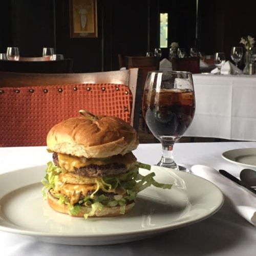 A gourmet burger with lettuce and cheese on a plate, accompanied by a glass of cola in an elegant restaurant setting.