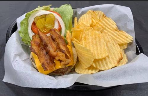 A cheeseburger topped with bacon, lettuce, tomato, and pickles, served with a side of ridged potato chips.