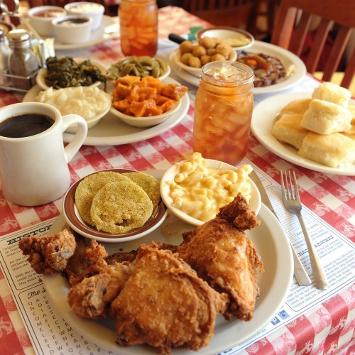 A table set with fried chicken, macaroni and cheese, greens, biscuits, and iced tea, all on a checkered tablecloth.
