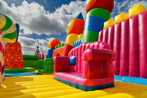 A colorful inflatable bounce house with various shapes and a pink couch in the center under a cloudy sky.