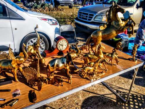 A table displaying various golden animal figurines and a clock, with a white car parked nearby.
