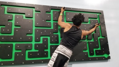A person climbs a textured wall with green patterns, using handholds for support.