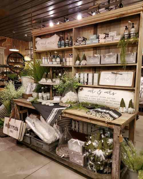 A rustic display featuring wedding-themed decor, candles, and gifts on wooden shelves in a cozy shop setting.