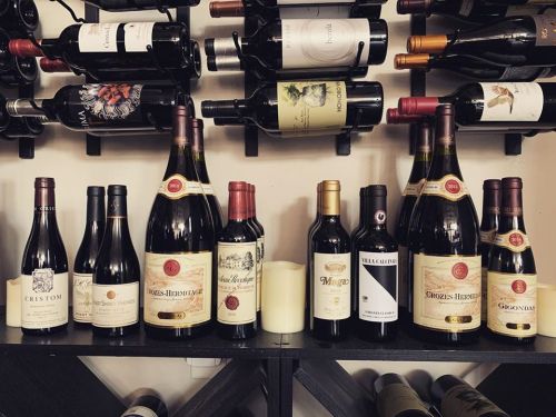 A collection of various wine bottles displayed on a wooden rack, featuring different brands and sizes.
