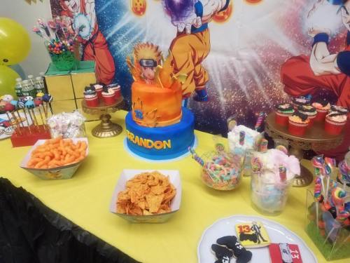 A colorful birthday table featuring a Naruto-themed cake, snacks, and candy, decorated with vibrant balloons and a backdrop.