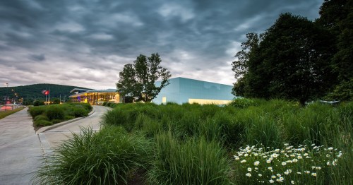 A modern building surrounded by lush greenery and flowers, under a cloudy sky.