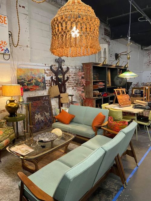 A cozy vintage furniture display featuring a light fixture, sofas, and various decor items in a rustic setting.