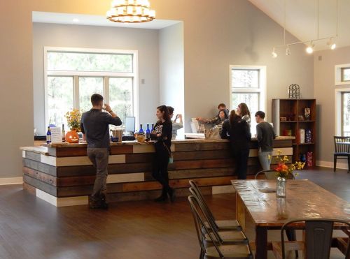 A cozy bar area with people socializing, wooden decor, and a table with flowers in a bright, spacious room.