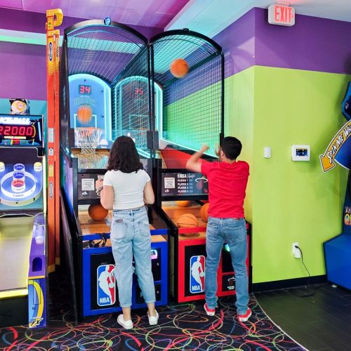 Two kids playing basketball arcade game, shooting hoops in a colorful game room.