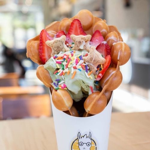 A delicious bubble waffle filled with mint ice cream, strawberries, sprinkles, and cute cookie decorations.